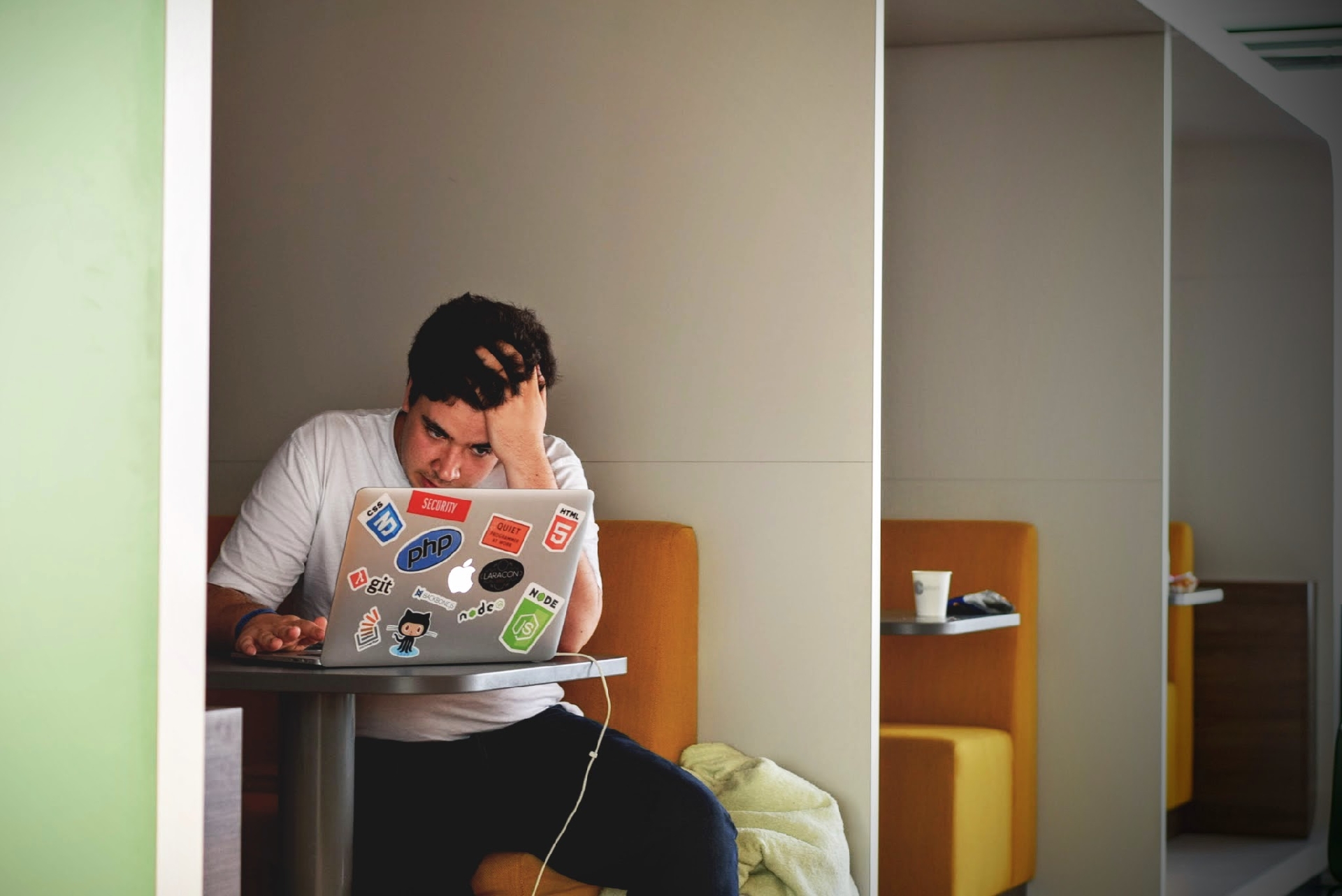 Man at laptop showing frustrated signs with hand on head, slumped over laptop.